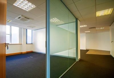Bright, empty office suite with glass partitioning and blue carpeting.