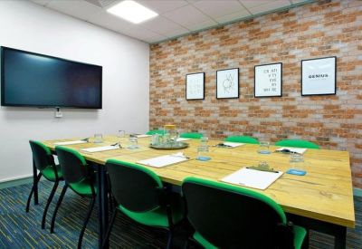 Meeting room featuring a wooden table, green chairs, and a brick-effect feature wall.
