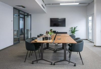 Sleek meeting room with a wooden table, grey chairs, and a wall-mounted screen.