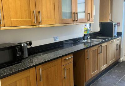 Modern communal kitchen area with wooden cabinetry and black granite countertops.