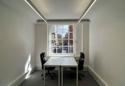 Narrow two-person office suite with white desks and long overhead linear lighting.