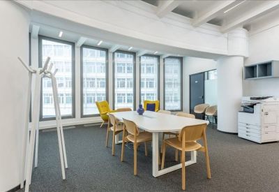 Spacious communal breakout area with a large white table, wooden chairs, and yellow armchairs.