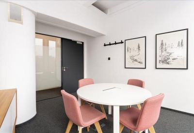 Small conference room with a round white table, pink chairs, and minimalist framed sketches.
