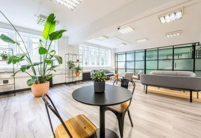 Spacious open-plan coworking space with a round table, wooden chairs, and large windows.