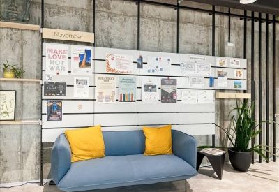 Informal lounge area with a blue sofa and yellow cushions against a notice board.