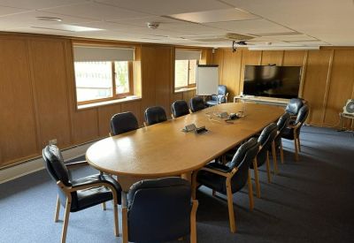 Wood-panelled boardroom featuring a large oval table and wall-mounted screen.