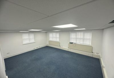 Spacious open-plan office with blue carpet and multiple windows.