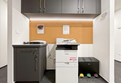 Office printing station with a large multifunction copier and grey storage cabinetry.