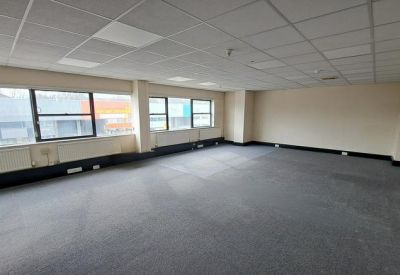 Spacious open-plan office with grey carpeting and large windows overlooking the street.