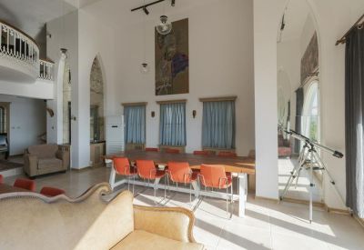 Spacious communal lounge with high ceilings, orange chairs, a large wooden table, and a telescope.