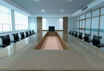 Modern conference room with a long glass table and rows of black ergonomic chairs.