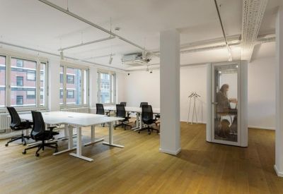 Bright open-plan workspace featuring white desks and a private glass phone booth.