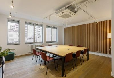 Large square wooden meeting table surrounded by red chairs and a slatted wood feature wall.