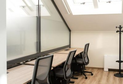 Modern workspace with several desks, ergonomic mesh chairs, and large slanted windows.