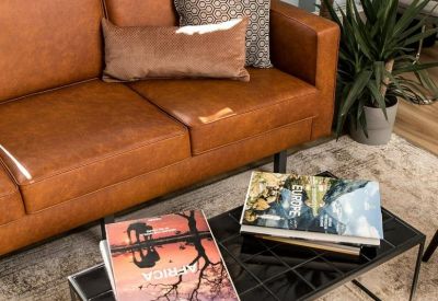 Lounge area with a tan leather sofa, patterned pillows, and a black coffee table with books.
