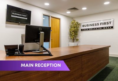 Modern wooden reception desk with branded signage and a large wall-mounted monitor.