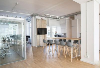 Modern communal kitchen and breakout area with high stools and a large wooden bar table.