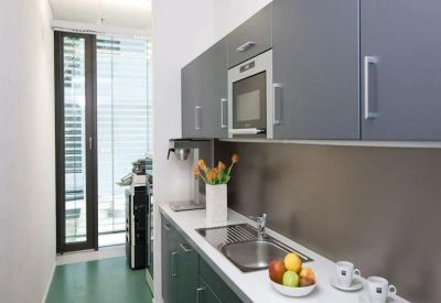 Modern compact kitchen featuring dark grey cabinetry and a white countertop with fruit and coffee.