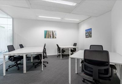 Open-plan office space with multiple white desks, black chairs, and natural light.