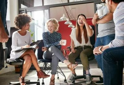 Spacious communal breakout area with diverse group seated on office chairs and stools.