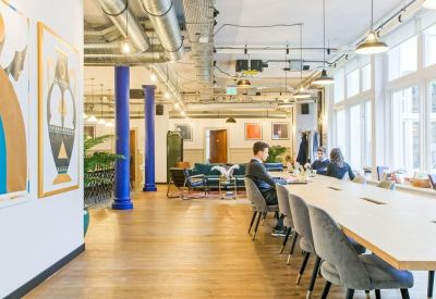 Bright open-plan coworking space with long communal tables and blue accent pillars.