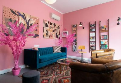 Vibrant pink lounge area with a teal sofa, velvet armchairs, and colorful wall art.