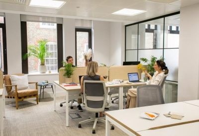 Bright open-plan office featuring white desks, ergonomic chairs, and large windows with street views.