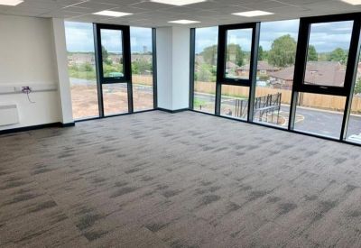 Spacious, empty office area with grey patterned carpeting and corner windows overlooking the street.
