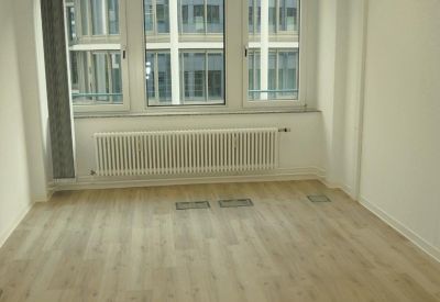 Empty office room with light wood flooring, a white radiator, and natural light.