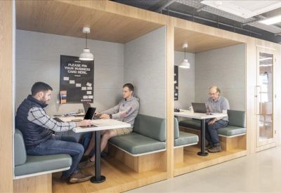 Modern plywood coworking booths with grey seating and individual lighting.