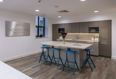 Modern communal kitchen with a large island, blue bar stools, and grey cabinetry.