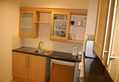 Compact communal kitchen area with light wood cabinetry and a black countertop.
