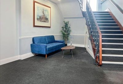 Reception area with a blue velvet sofa, a small coffee table, and a staircase with a wooden banister.