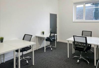 Shared office space with multiple white desks, black mesh chairs, and grey carpeting.
