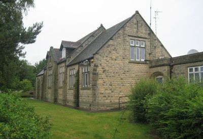 Rear corner of a traditional stone structure with green lawn and shrubbery.