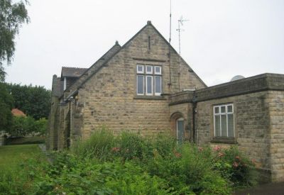 Stone building exterior featuring a mix of pitched and flat roof sections with lush foliage.