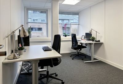 Bright two-person office with white desks, task lamps, and natural light from large windows.