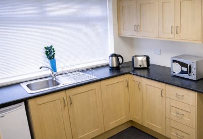 Communal kitchen area with light wood cabinetry, black countertops, and a microwave.