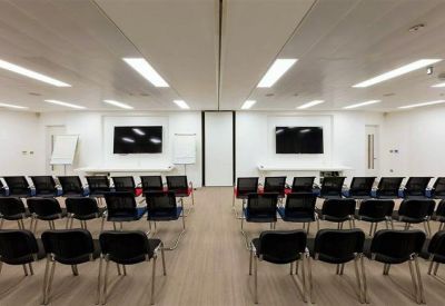 Large conference hall with multiple rows of black chairs facing presentation screens.