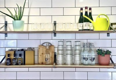 Stylish kitchen shelving with white subway tiles, plants, glassware, and a bright yellow watering can.