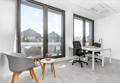 Small consultation area with grey armchairs, a wooden side table, and a glass-walled office view.