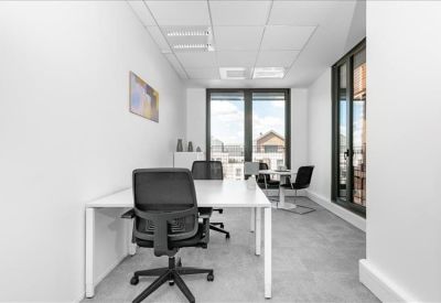 Bright private office featuring a white desk, black ergonomic chairs, and large windows.