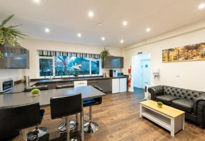 Communal kitchen and breakout area with a dark leather sofa and wooden flooring.