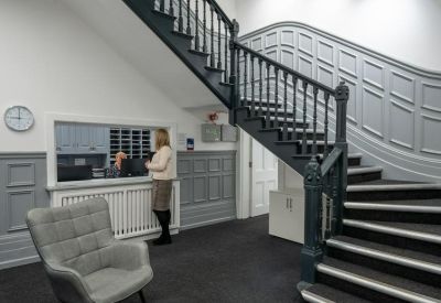 Reception area featuring a dark wooden staircase with ornate bannisters and a grey armchair.