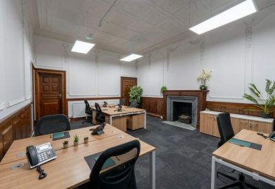 Shared office space with wooden desks, ergonomic chairs, and a classic fireplace feature.