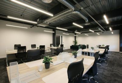 Bright open-plan office with light wood desks and exposed ductwork.