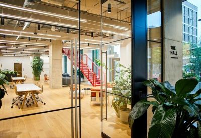 Bright coworking space with wooden floors, indoor plants, and a vibrant red staircase.