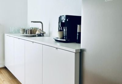 Communal kitchen area with white cabinets, a coffee machine, and integrated sink.