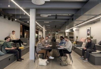 Modern coworking space with tiered bench seating, individual desks, and exposed ceiling pipes.