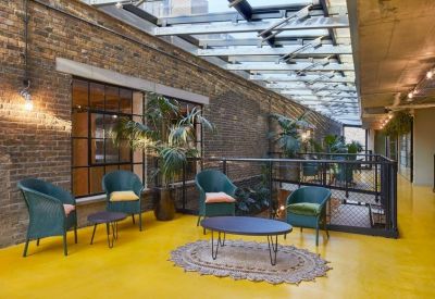 Mezzanine lounge area with blue armchairs, yellow flooring, and a glass ceiling.